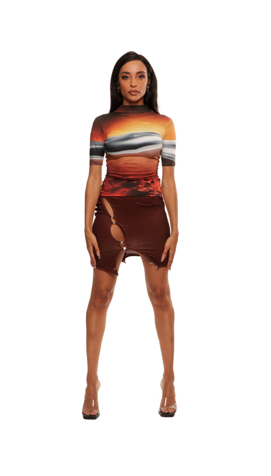 Woman wearing a brown skirt with cutouts and snaps paired with a short sleeve tech tee featuring a sunset on mars print and chrome metal detail across chest with QR logo